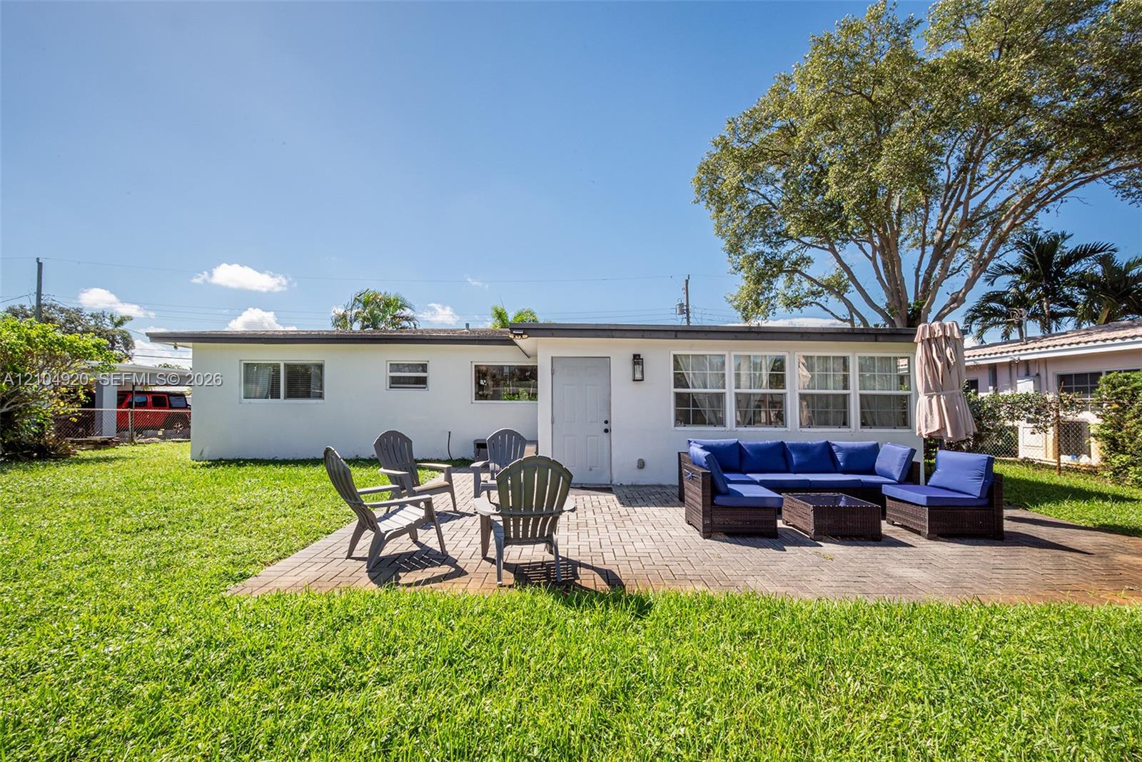 Rear exterior featuring a paver patio, mature trees, and a level lawn area