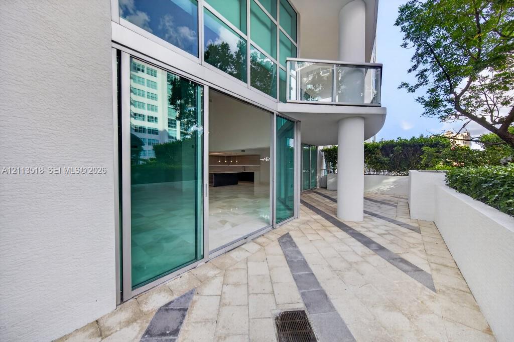 Expansive stone-paved terrace with contrasting linear accents, floor-to-ceiling glass sliding doors, elevated glass-paneled balcony, and structural co