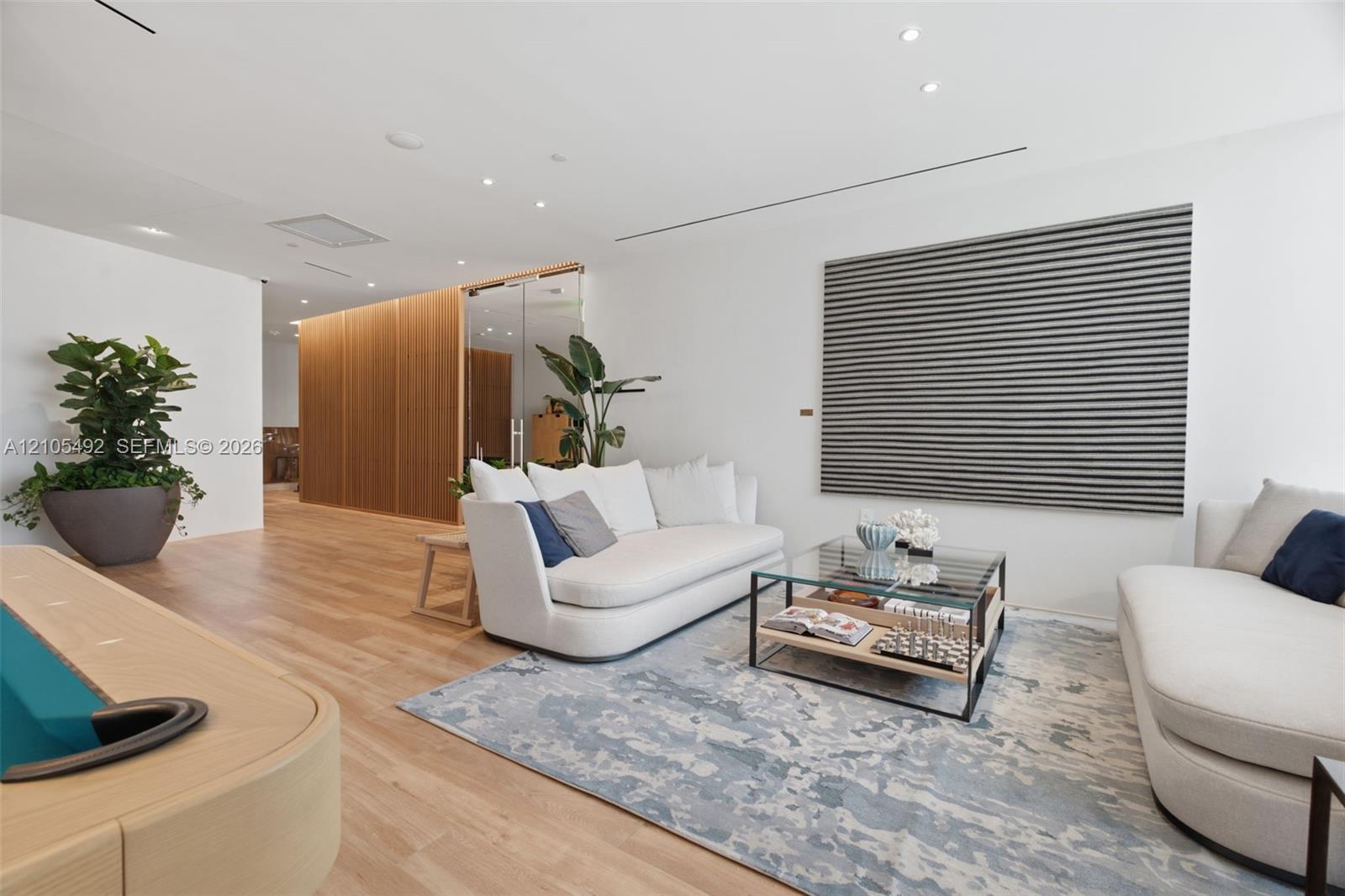 Living space featuring wood-finish flooring, recessed lighting, vertical wood wall paneling, and floor-to-ceiling glass wall partitioning