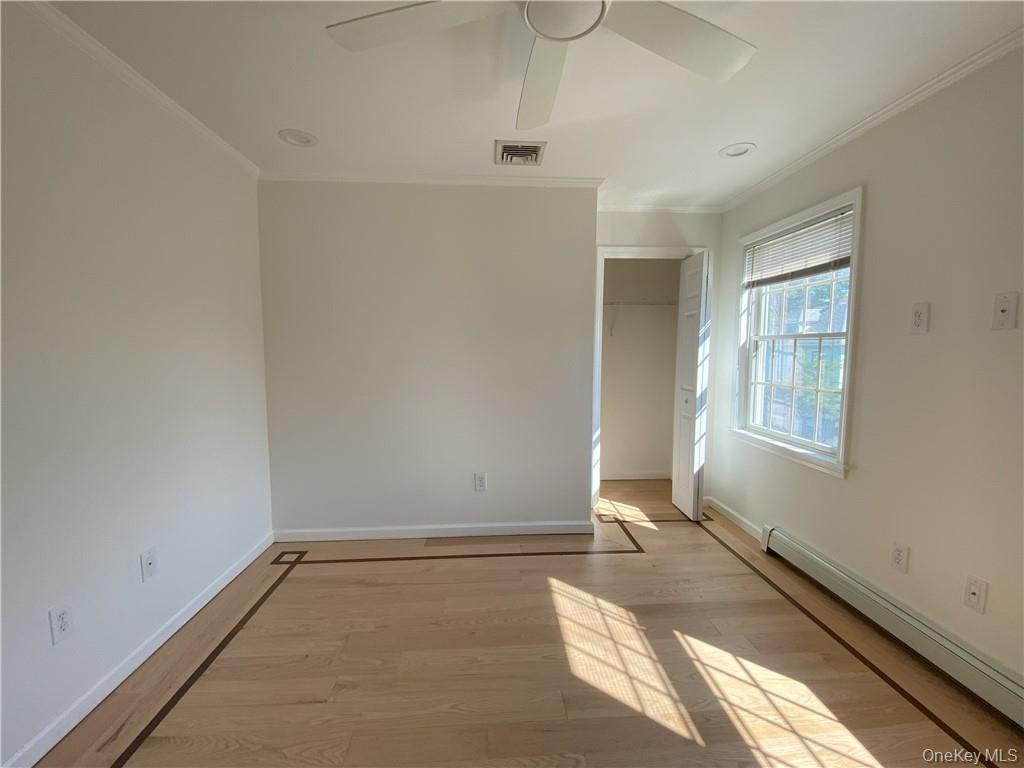 Unfurnished bedroom featuring a closet, baseboard heating, ceiling fan, wood-type flooring, and ornamental molding