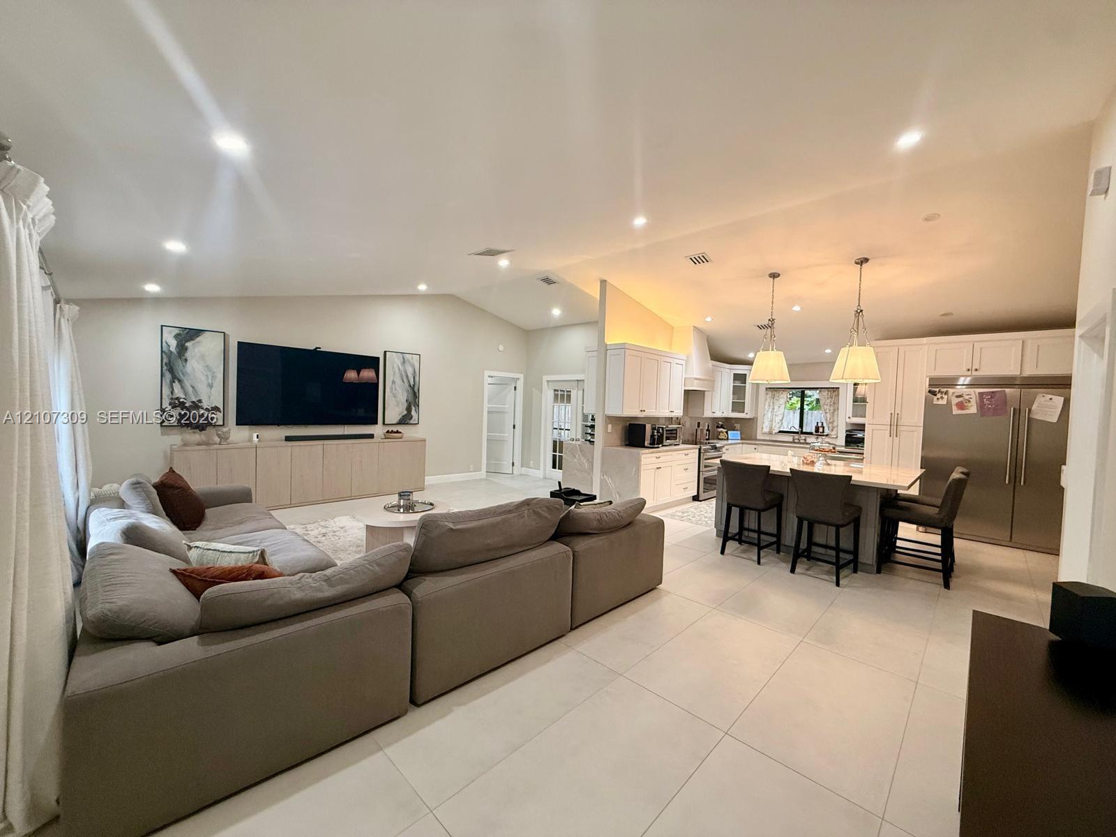 Open-concept interior featuring vaulted ceilings, light-toned large-format tile flooring, a kitchen island with stone countertops, and recessed lighti