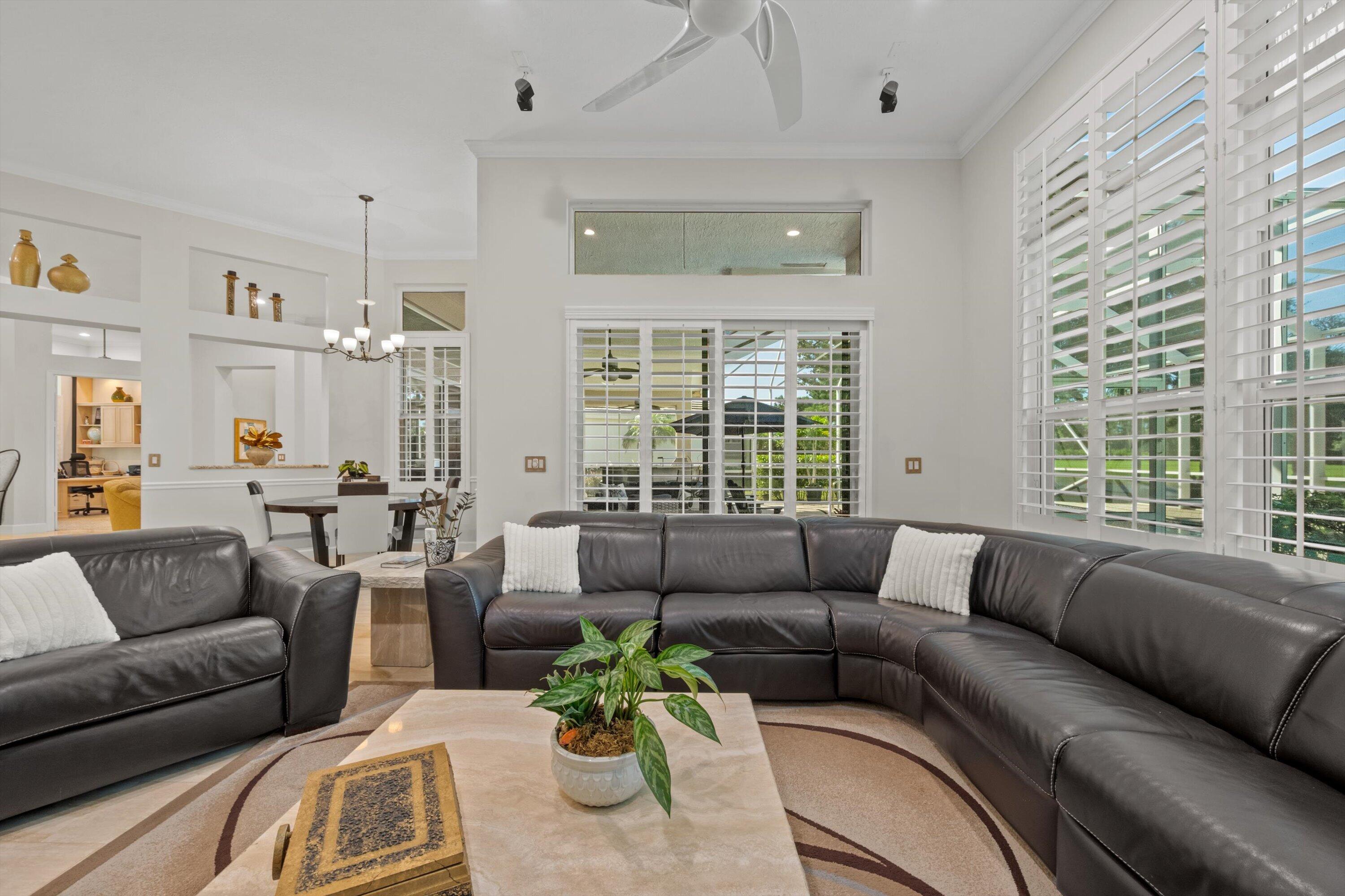 High ceilings featuring a multi-blade ceiling fan, expansive transom windows, built-in wall niches, custom plantation shutters, and sliding glass door