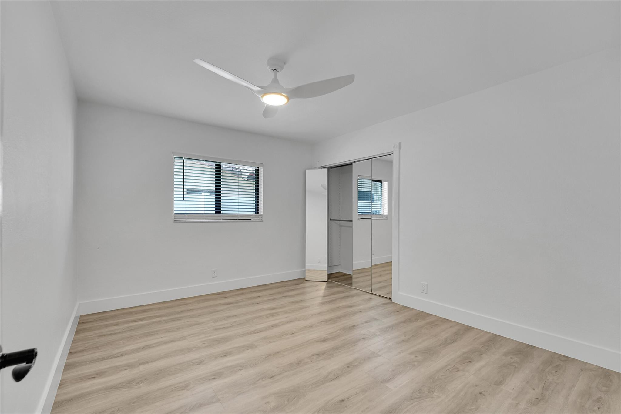 Spacious room featuring wood-finish flooring, a contemporary ceiling fan, and mirrored closet doors