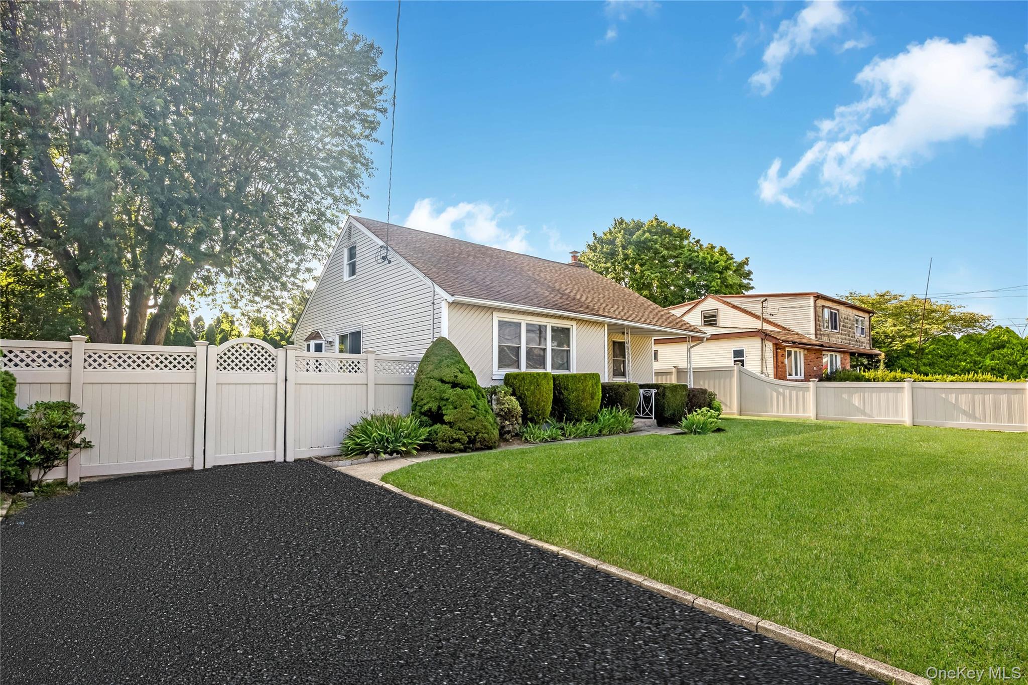 Paved driveway with white lattice-top fencing and gate, mature landscaping, and a manicured lawn