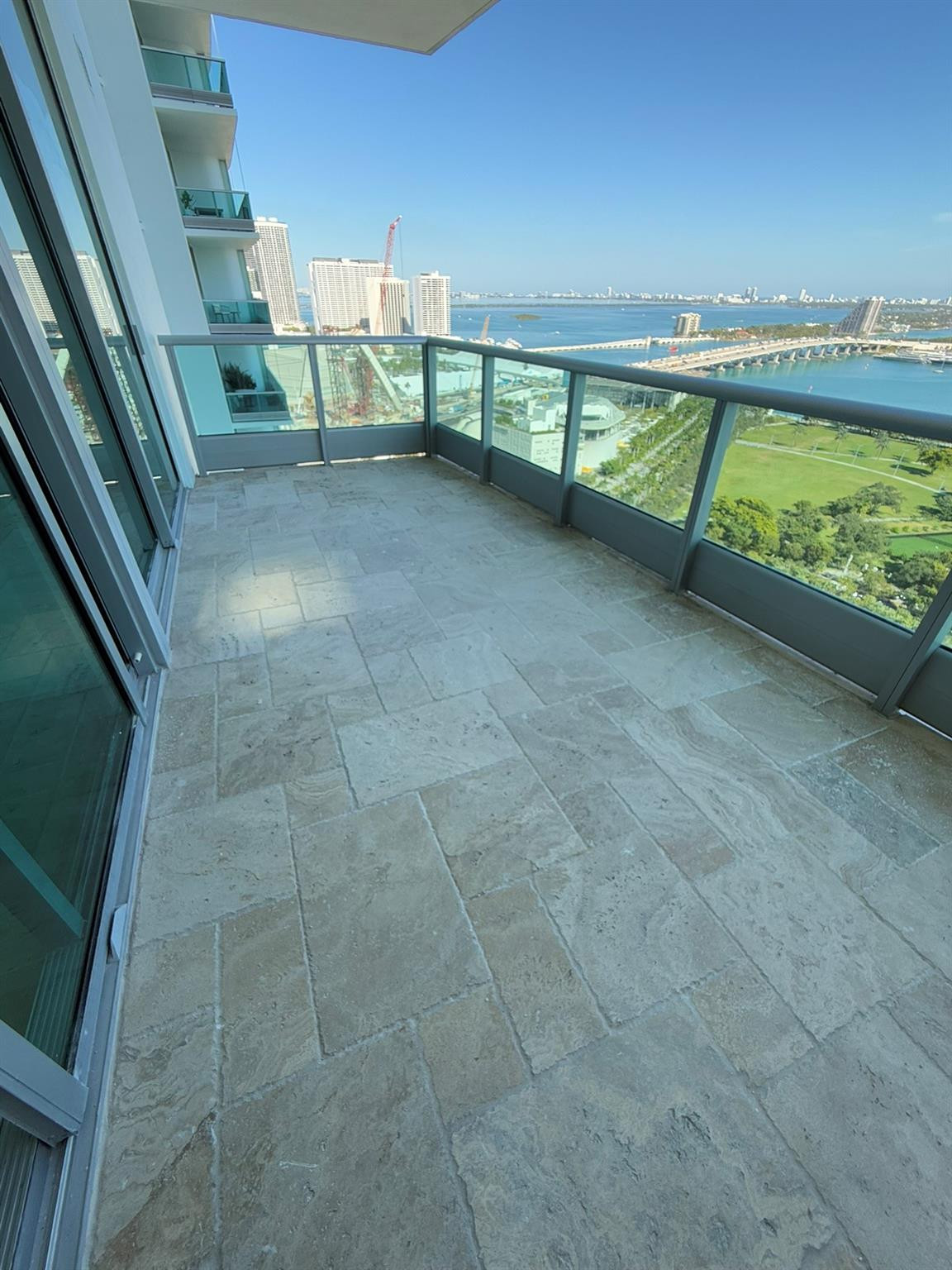 Spacious balcony featuring stone tile flooring, clear glass railings, and expansive water scenery