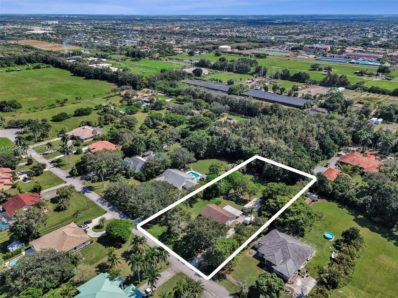 Aerial view of expansive lot featuring mature tree cover and a structure with a pitched roof