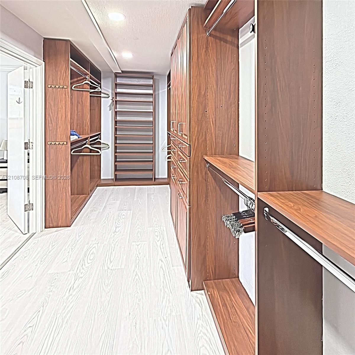 Custom walk-in closet featuring extensive wood-finish cabinetry, built-in shelving, integrated hanging rods, recessed ceiling lighting, and light-tone