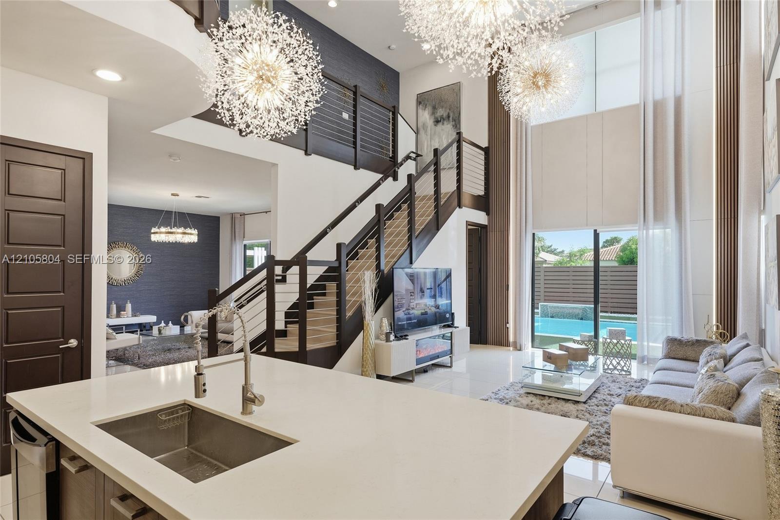 Double-height ceiling, open-plan interior featuring a floating staircase with cable railing, expansive floor-to-ceiling windows, dual sputnik-style ch
