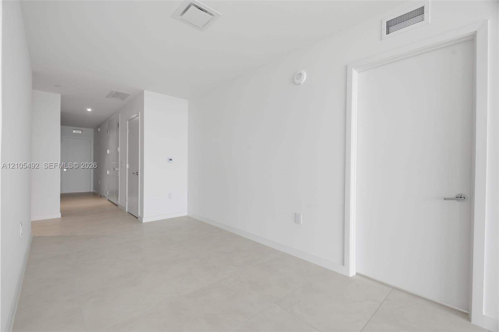 Interior space featuring large-format ceramic tile flooring, smooth white walls, solid-core interior doors with satin nickel hardware, and recessed LE