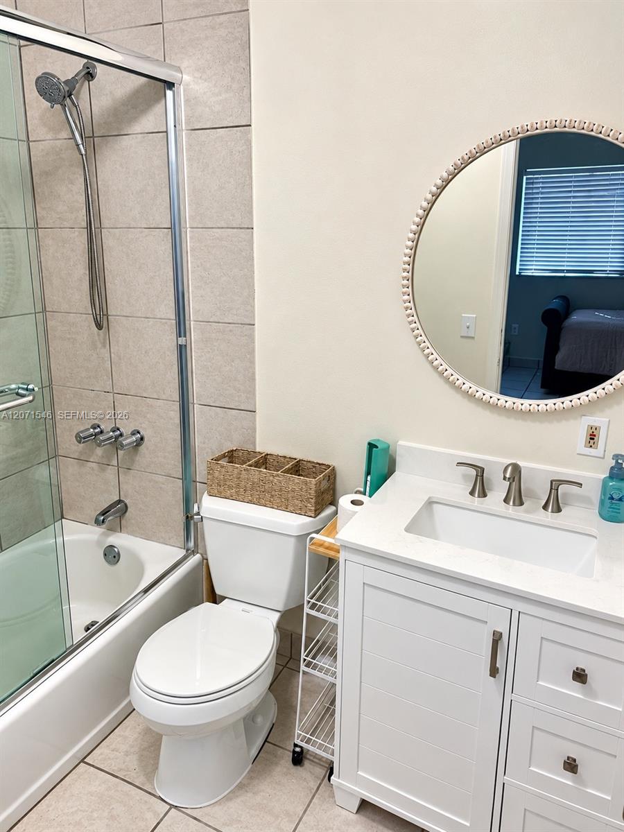 White vanity featuring a solid surface countertop, rectangular undermount sink, and brushed-finish fixtures, paired with a glass-enclosed shower with 