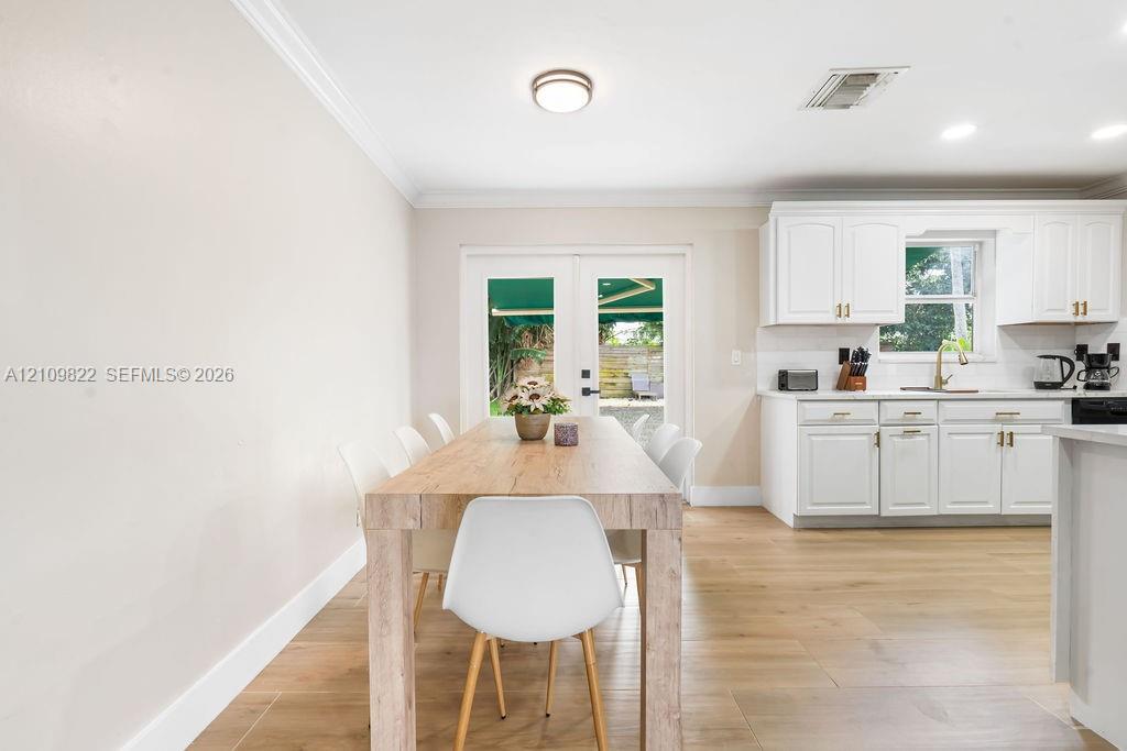 White cabinetry, wood-finish flooring, crown molding, and glass-paneled double doors featuring matte black hardware