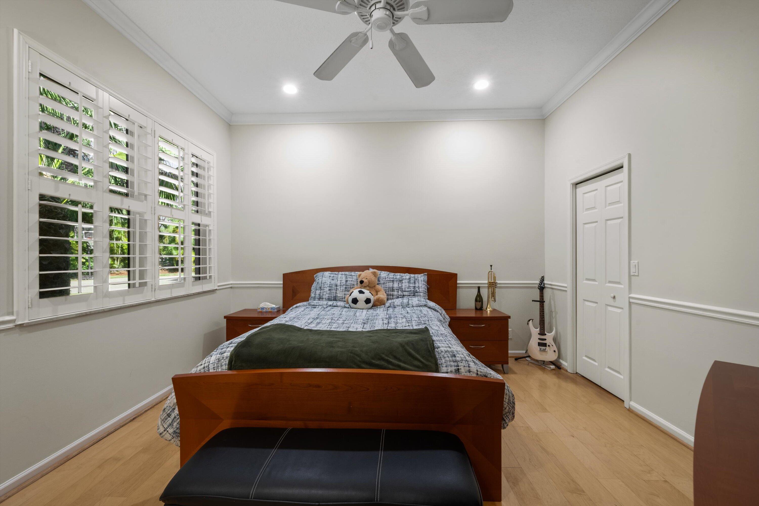 Room featuring wood-finish flooring, crown molding, chair rail trim, plantation shutters, and a ceiling fan