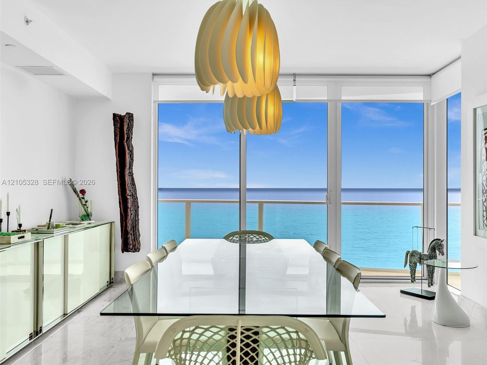 Elegant dining area featuring floor-to-ceiling glass doors and windows, large-format tile flooring, contemporary pendant lighting, and a glass-top din