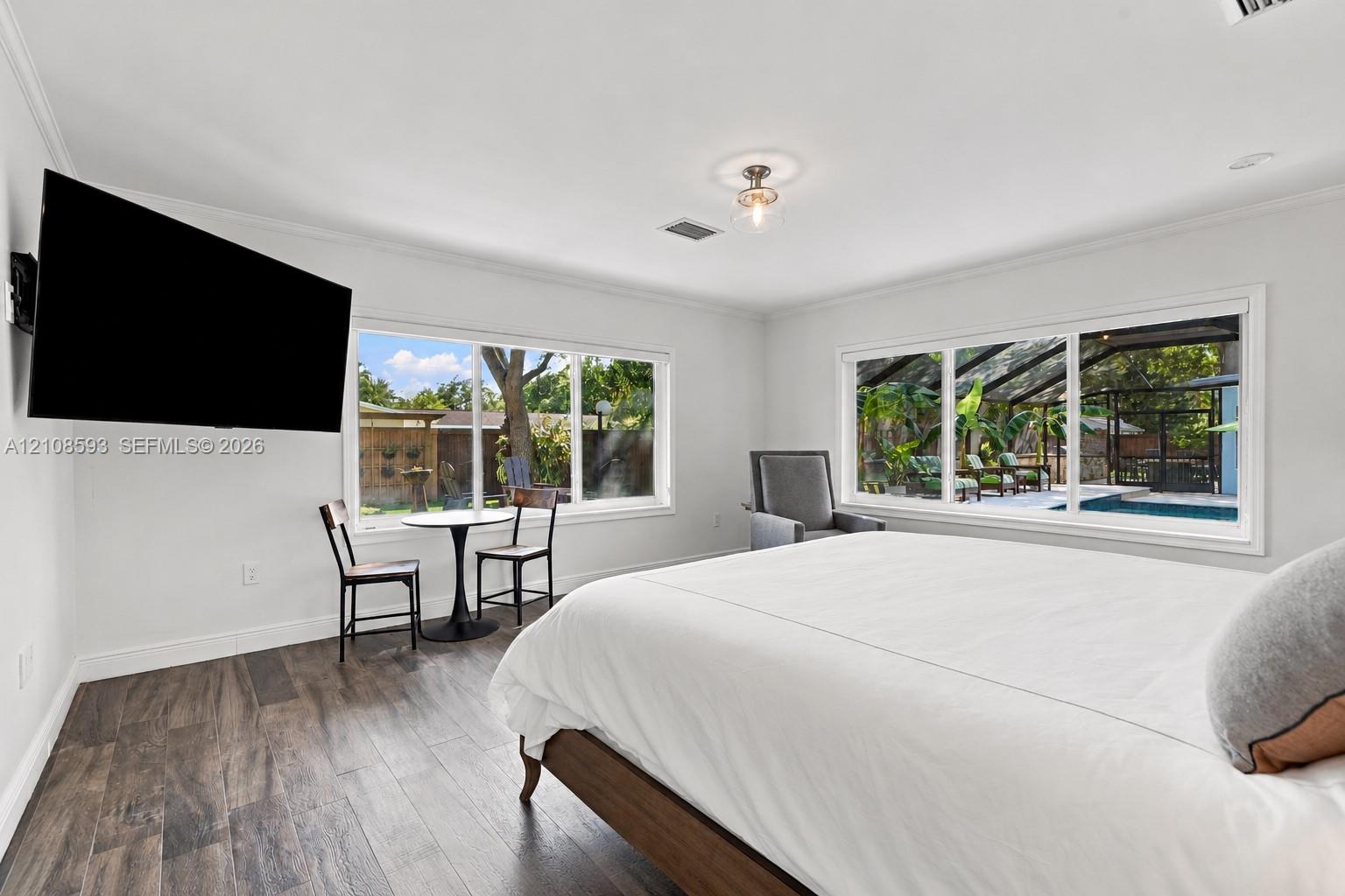 Neutral-toned interior featuring wood-finish flooring, dual large-scale windows with natural light, a semi-flush mount ceiling fixture, and crown mold