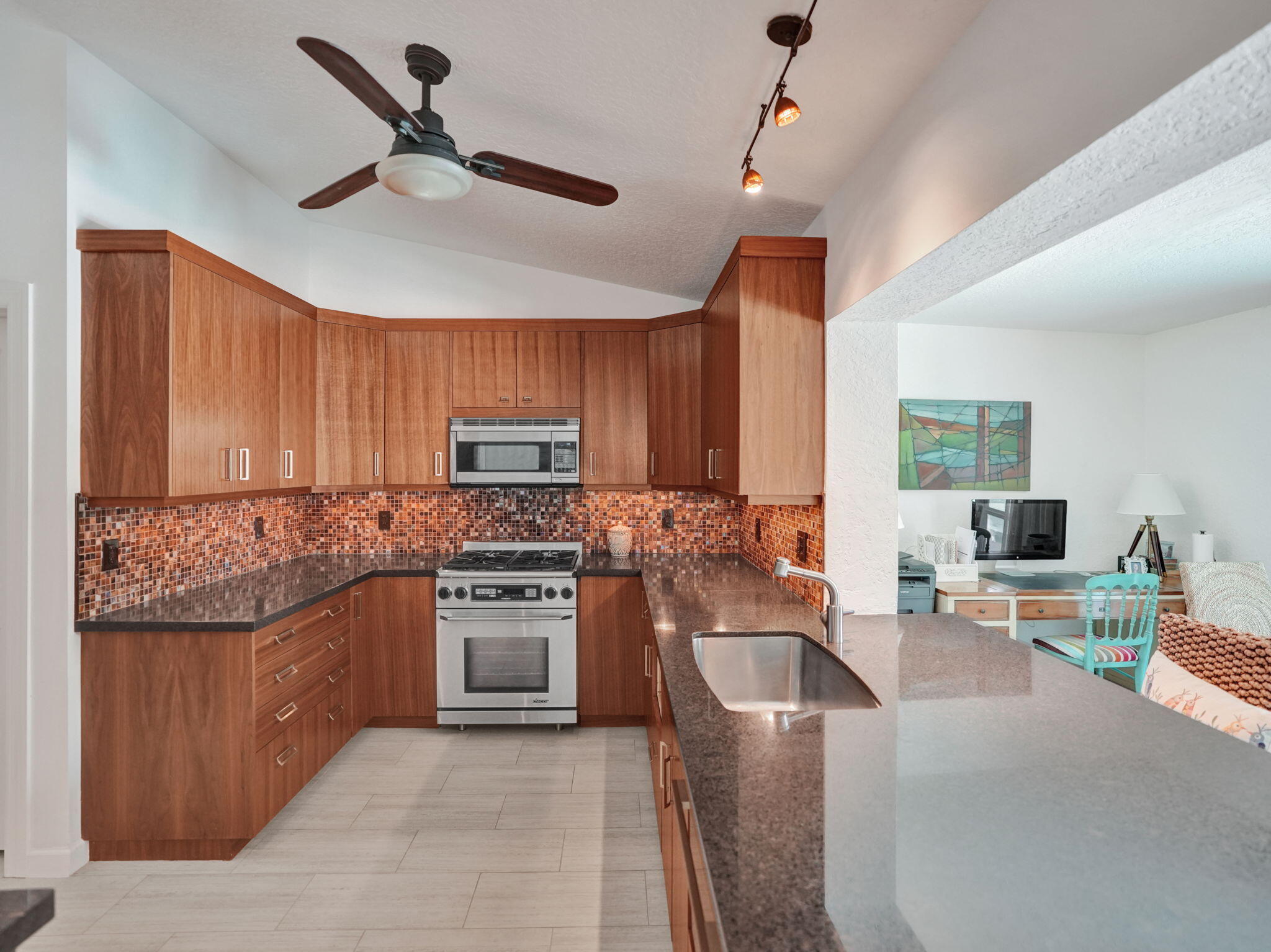 Kitchen featuring wood-finish cabinetry, mosaic tile backsplash, stainless steel range, and an integrated stainless steel sink within a stone countert