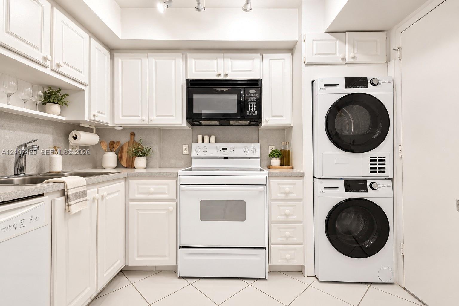 Kitchen featuring shaker-style cabinetry, solid-surface countertops, stainless steel sink with high-arc faucet, integrated laundry center, and tile fl