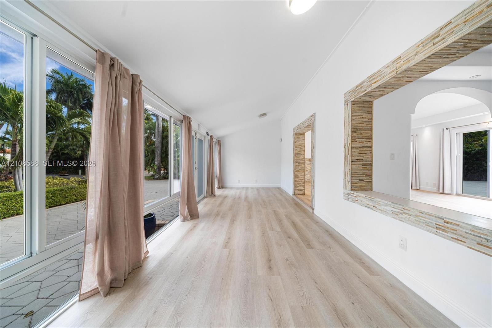 Light-filled interior featuring expansive floor-to-ceiling glass sliding doors, wood-finish flooring, a vaulted ceiling, and stacked-stone decorative 