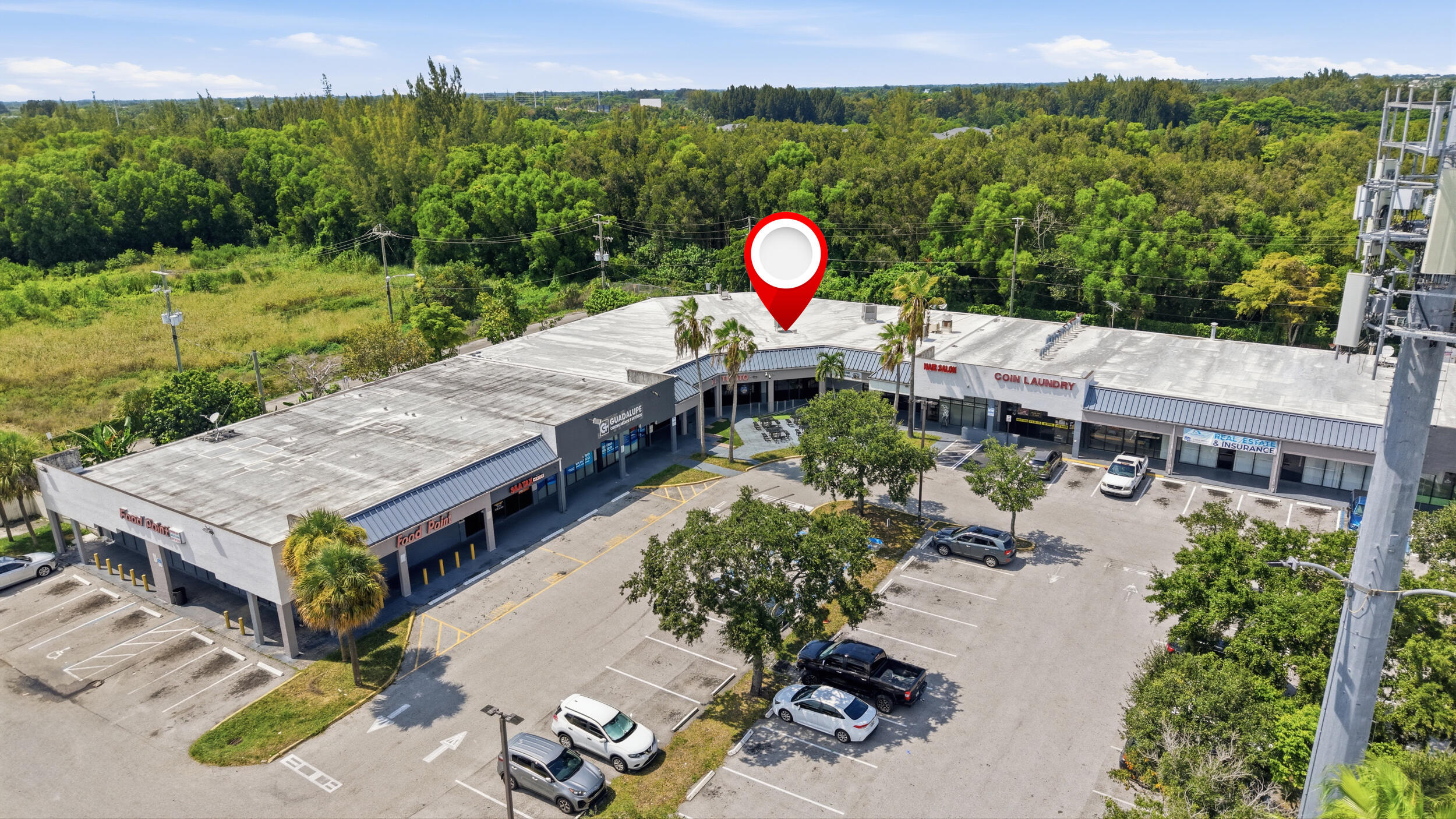 Commercial plaza featuring a U-shaped building design, expansive paved parking area, mature landscaping, and prominent signage space