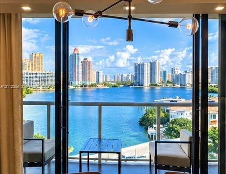 Floor-to-ceiling glass panel doors, metal-railing balcony, multi-arm metallic light fixture, and recessed lighting