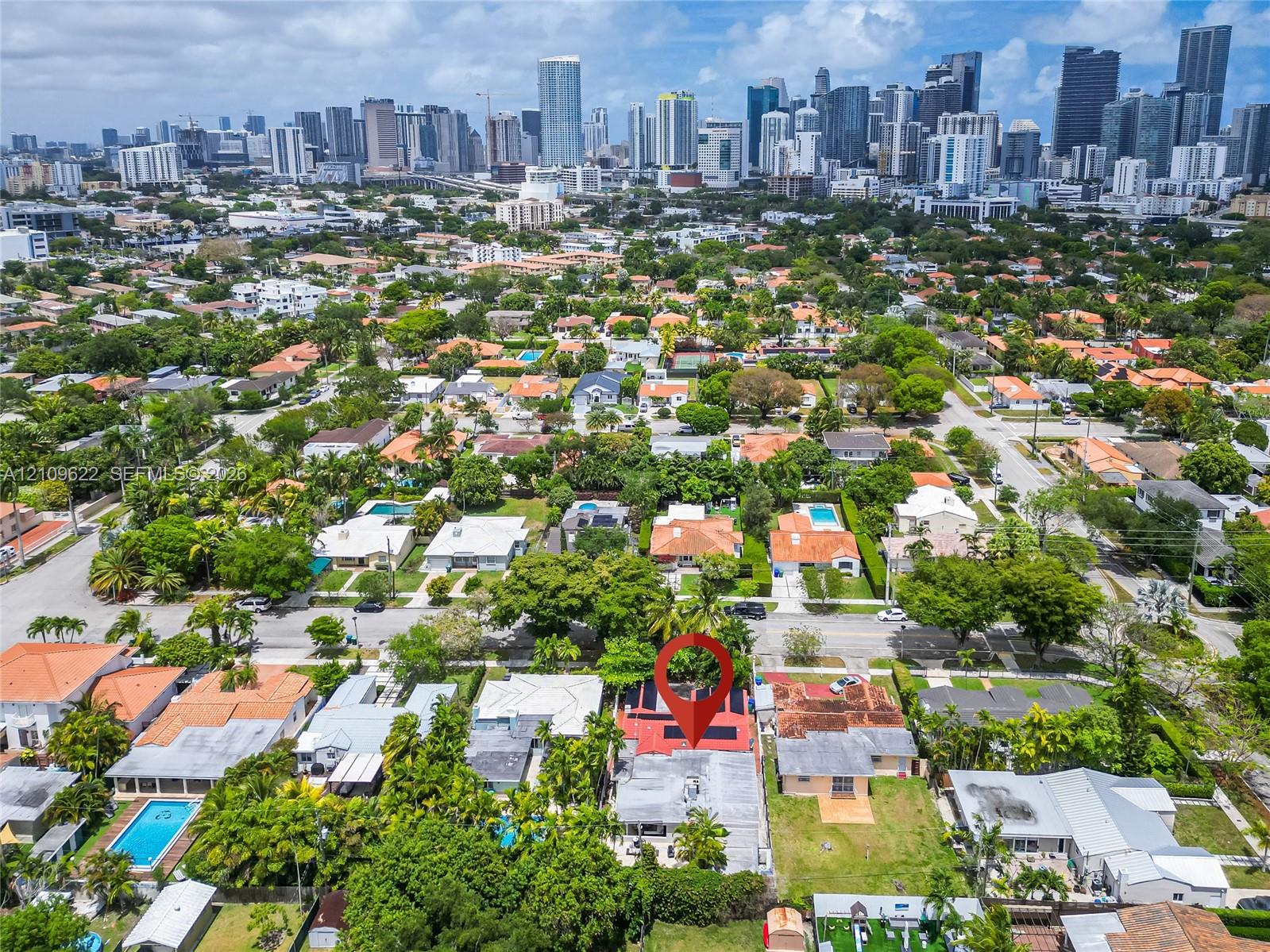 Aerial perspective of residential property featuring a flat roof with solar panel installation, mature landscaping, and an expansive cityscape backdro