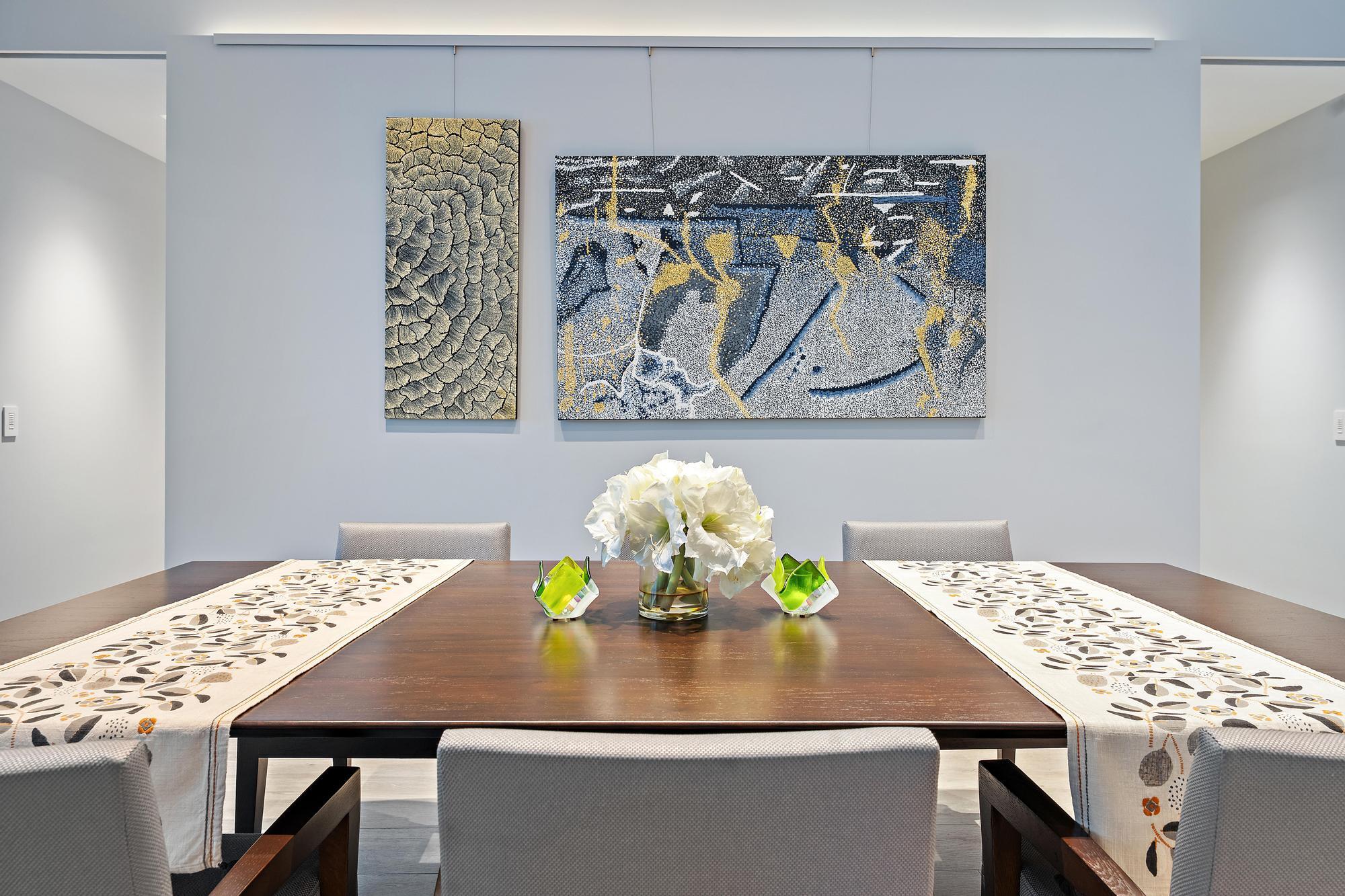 Wood-finish dining table with upholstered chairs, recessed lighting, and wall-mounted art display system