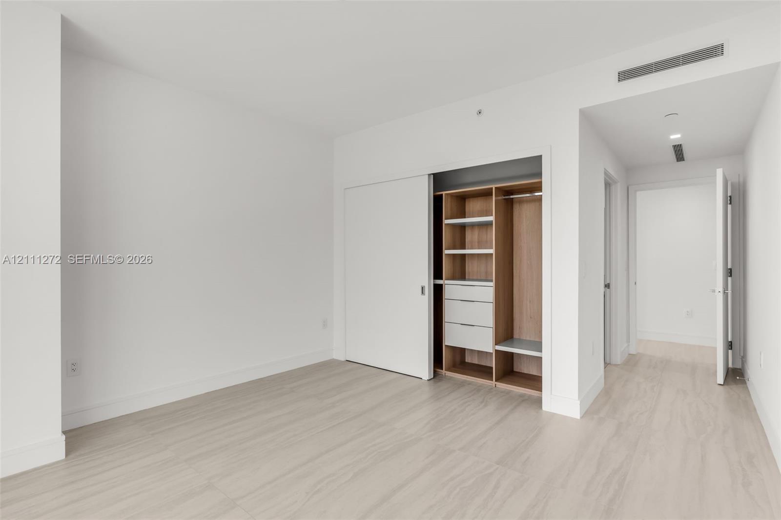 Room featuring neutral wall finishes, light wood-finish flooring, and a built-in closet system with integrated shelving and drawer storage behind a sl