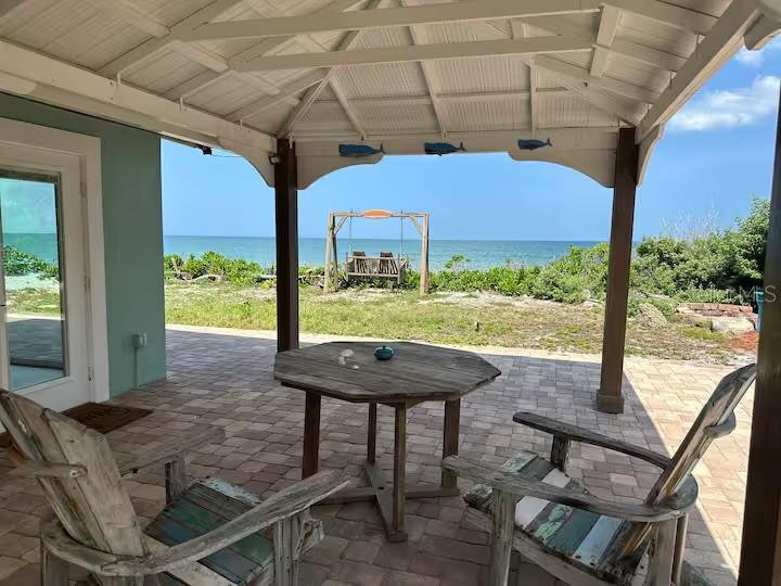 A cozy and shaded outdoor patio with two comfortable chairs and a small table set against a beautiful beachfront.