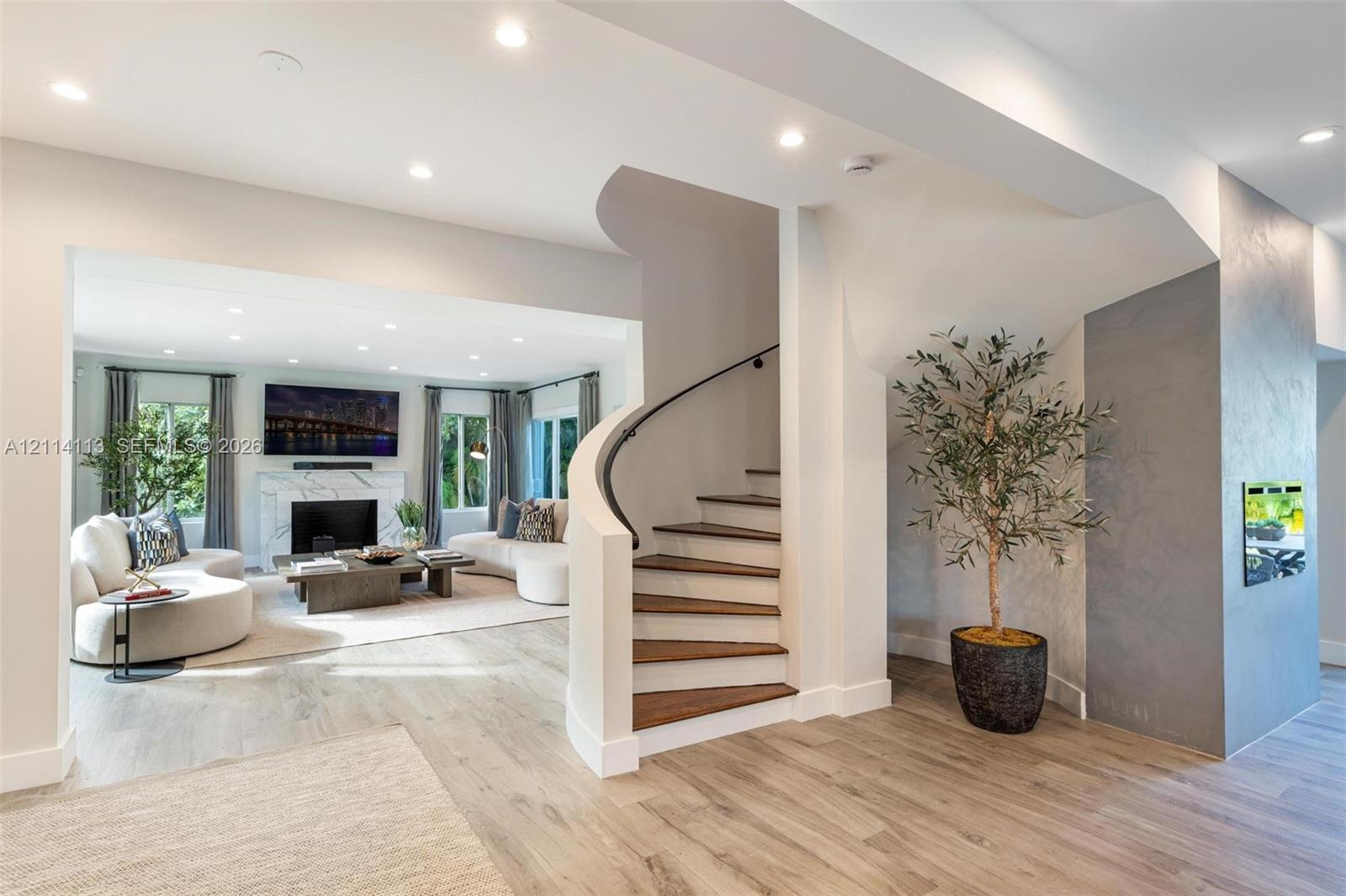 Curved staircase with wood treads and black metal handrail, fireplace with stone-surround, recessed lighting, and wood flooring