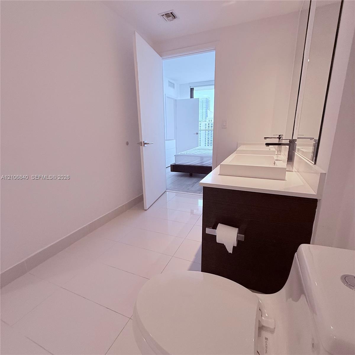 Bathroom featuring a dark wood-finish vanity with dual rectangular vessel sinks, light-toned stone countertop, polished tile flooring, and large-forma