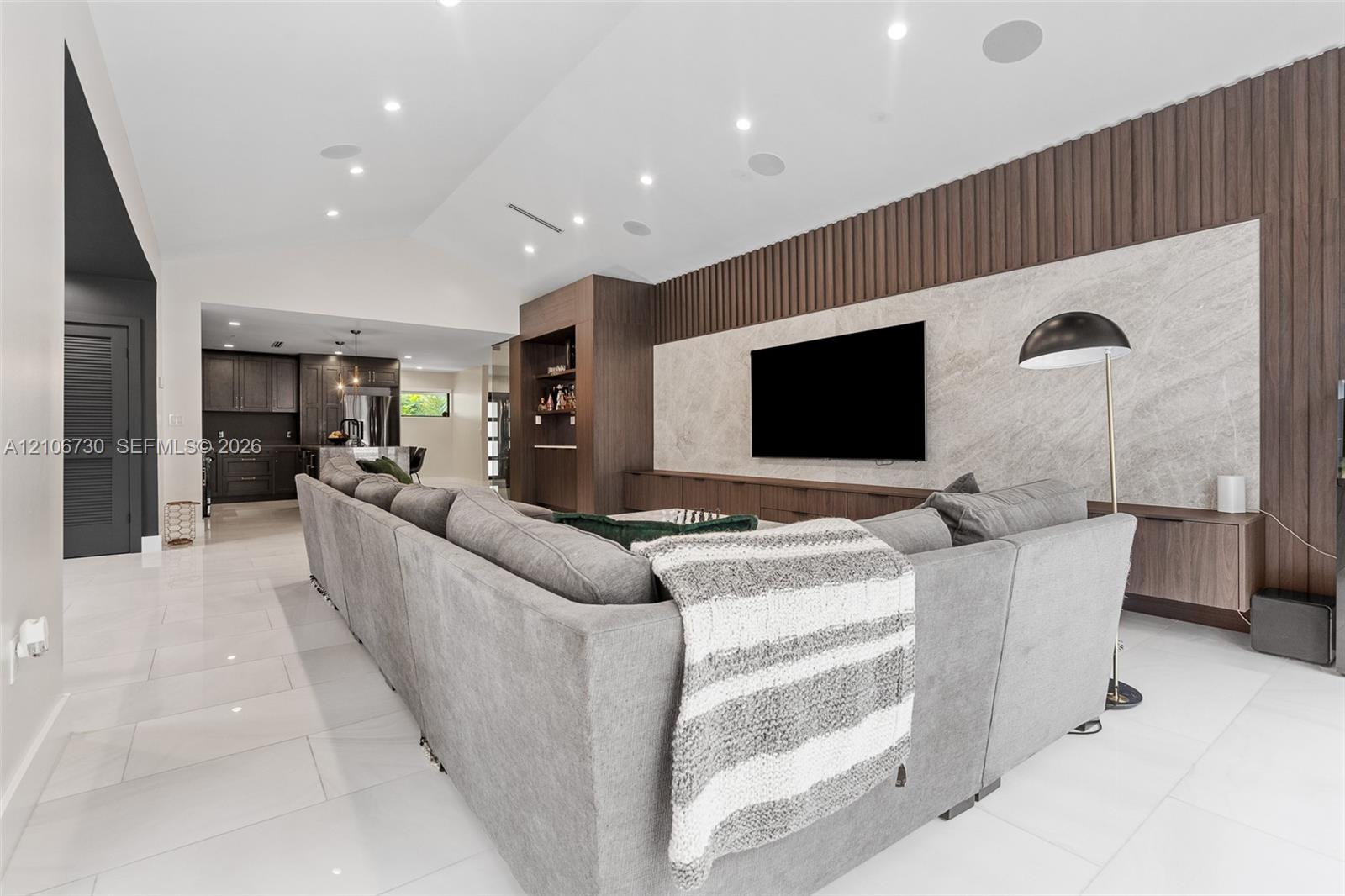 Vaulted ceilings, large-format tile flooring, recessed lighting, and a custom floor-to-ceiling accent wall featuring vertical wood-slat paneling with 