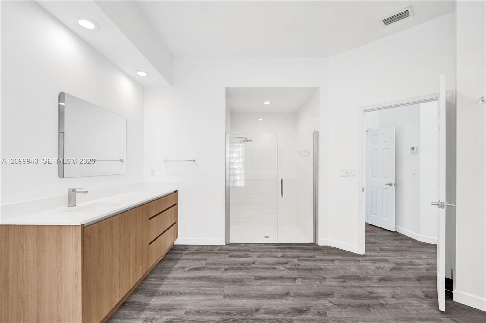 Bathroom featuring a wood-finish floating vanity with a solid-surface countertop, an integrated sink, a glass-enclosed shower, and wood-finish floorin