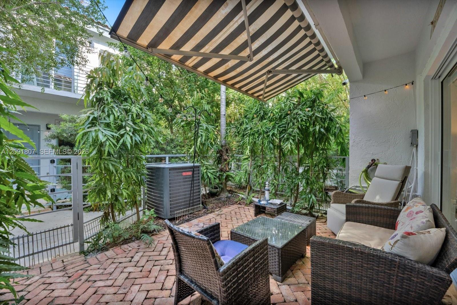 Outdoor patio featuring a herringbone-patterned brick floor, retractable striped awning, and metal perimeter fencing