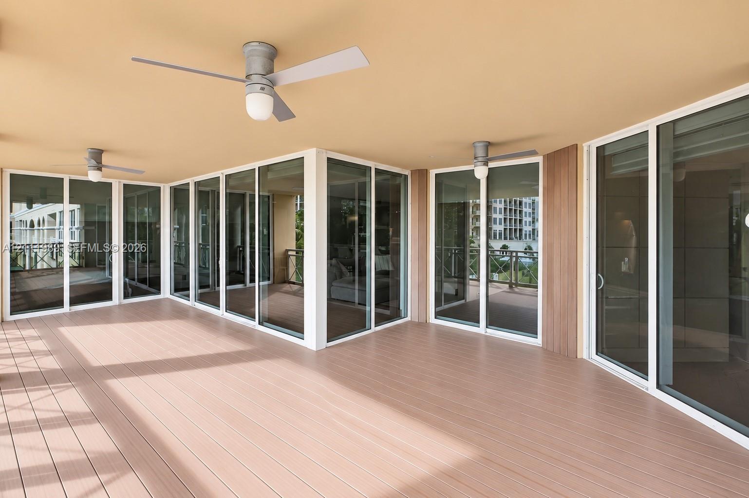Covered outdoor terrace featuring wood-finish decking, multiple glass sliding doors, and dual ceiling fans