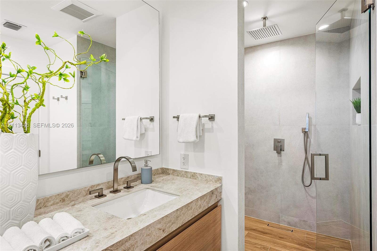 Bathroom featuring a stone-surface vanity with an integrated sink, wood-finish cabinetry, a large wall-mounted mirror, and a walk-in glass-enclosed sh