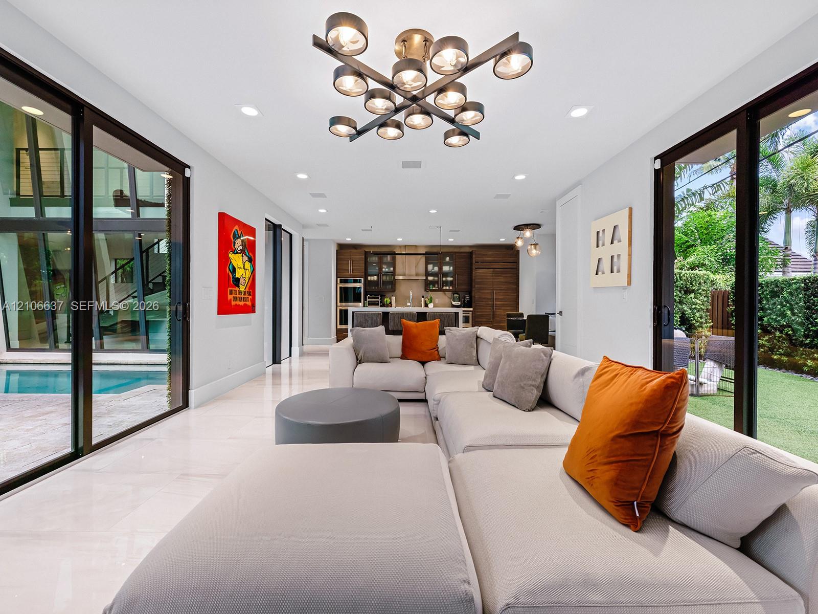 Open-concept interior featuring large-format tile flooring, multi-light geometric chandelier, recessed lighting, and floor-to-ceiling glass sliding do