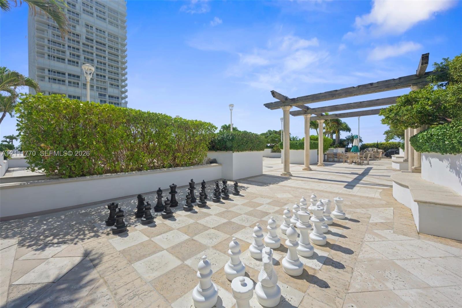 Outdoor terrace featuring stone tile flooring, a built-in pergola, custom raised planter boxes with manicured hedges, and a permanent oversized chess 