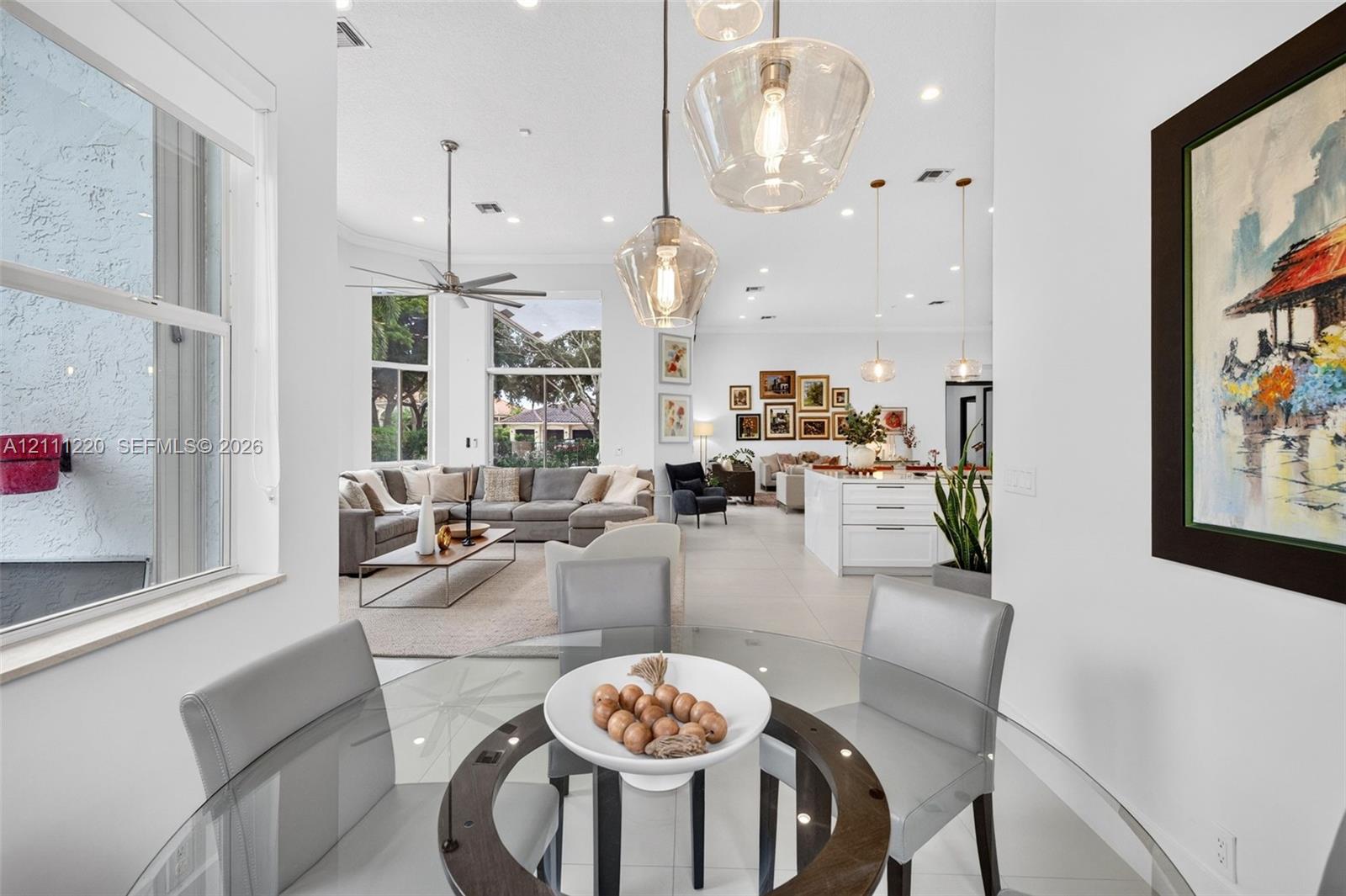Open-concept interior featuring large-format tile flooring, recessed lighting, expansive windows, and tiered glass pendant fixtures over the dining ar