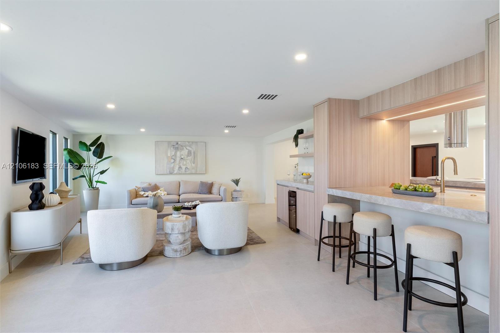 Open-concept space featuring light-toned cabinetry, a stone-surface breakfast bar with under-cabinet lighting, recessed ceiling lights, and tile floor