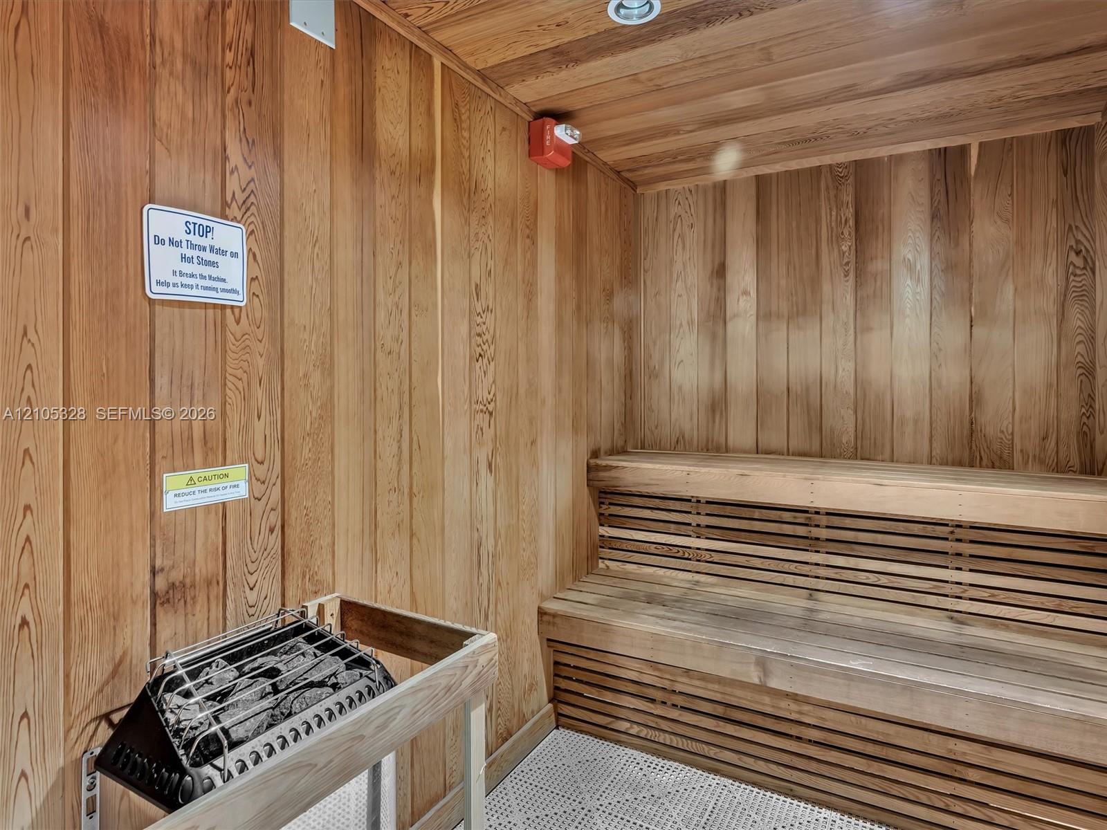 Wood-paneled sauna featuring built-in wood benches, a sauna heater with protective railing, and recessed ceiling lighting
