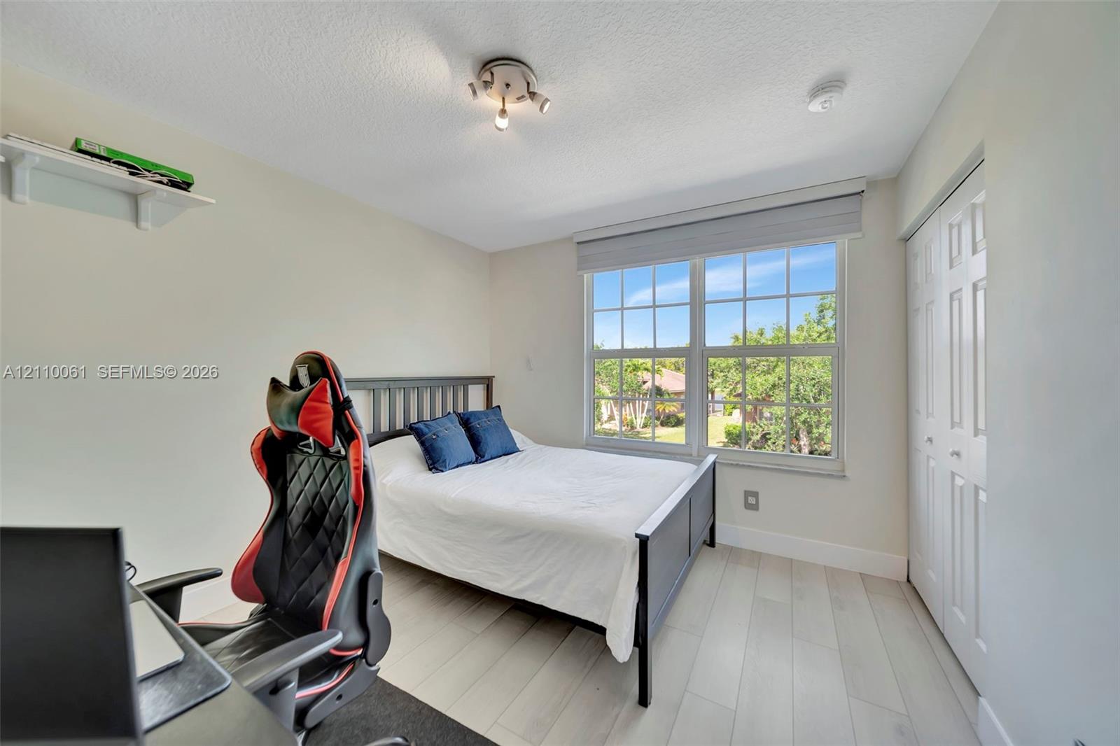Wood-finish flooring, multi-pane window with custom shade, built-in shelving, triple-bulb track lighting, and a bi-fold closet
