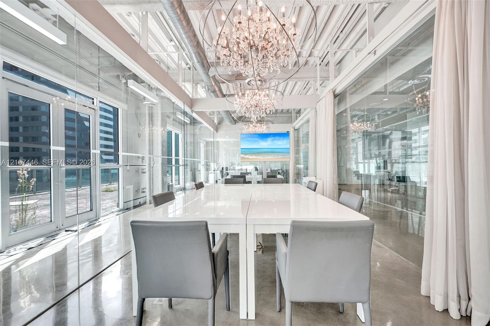 Exposed industrial ceiling with ductwork, expansive glass wall partitions, polished concrete flooring, multiple crystal chandeliers, and exterior glas