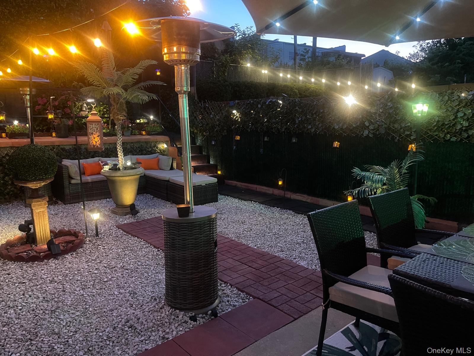 Landscaped outdoor area featuring gravel ground cover, brick paver pathways, perimeter hedging, and built-in patio lighting
