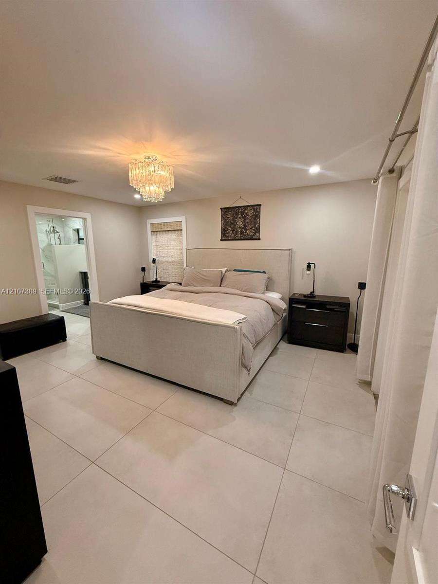 Neutral-toned large format tile flooring, crystal chandelier light fixture, recessed ceiling lighting, and window with woven shade