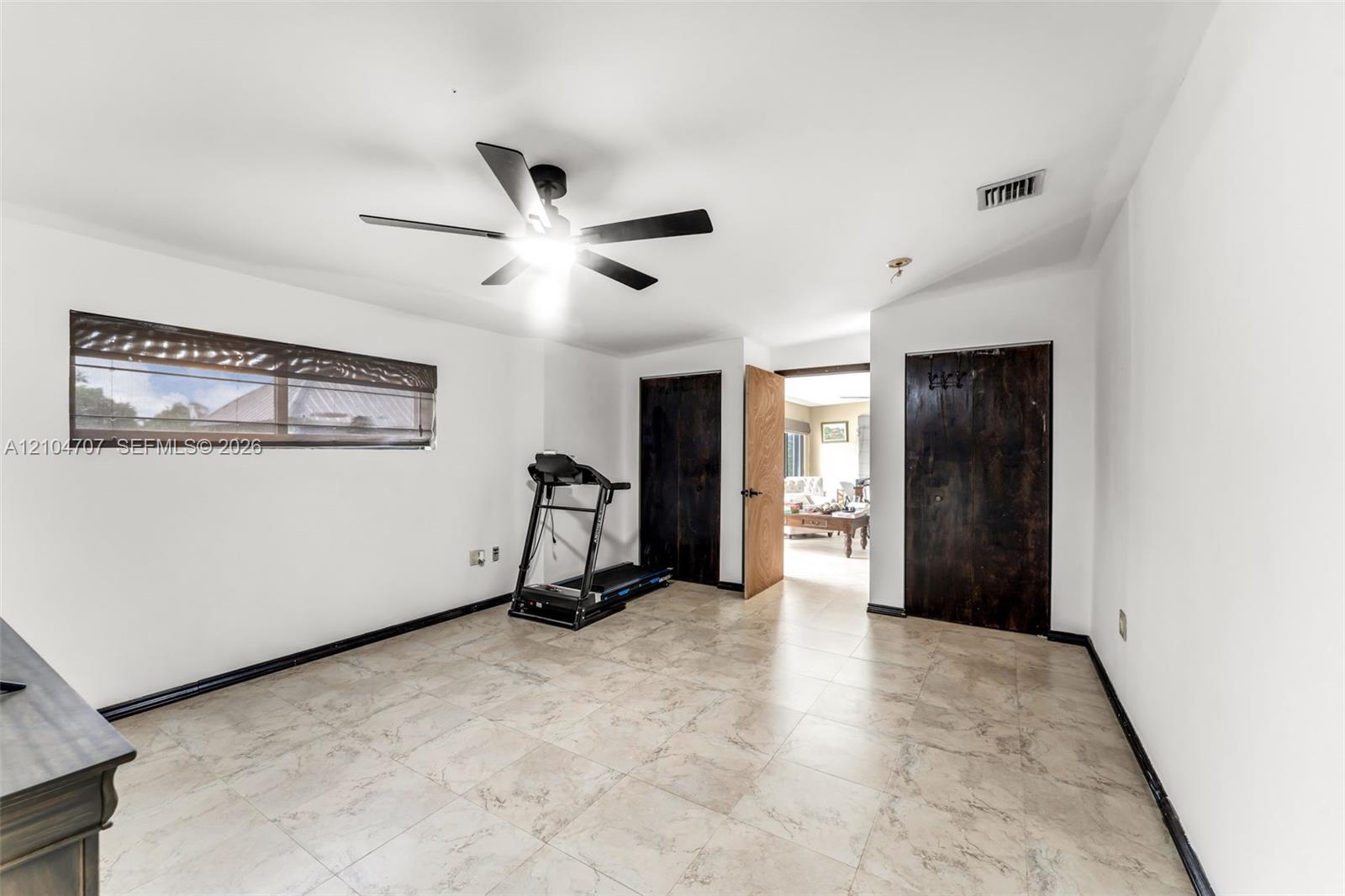 Room featuring tiled flooring, a multi-blade ceiling fan, and multiple windows finished with roman shades
