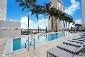 Rectangular lap pool featuring stone-tile decking, stainless steel ladder railings, and perimeter palm trees