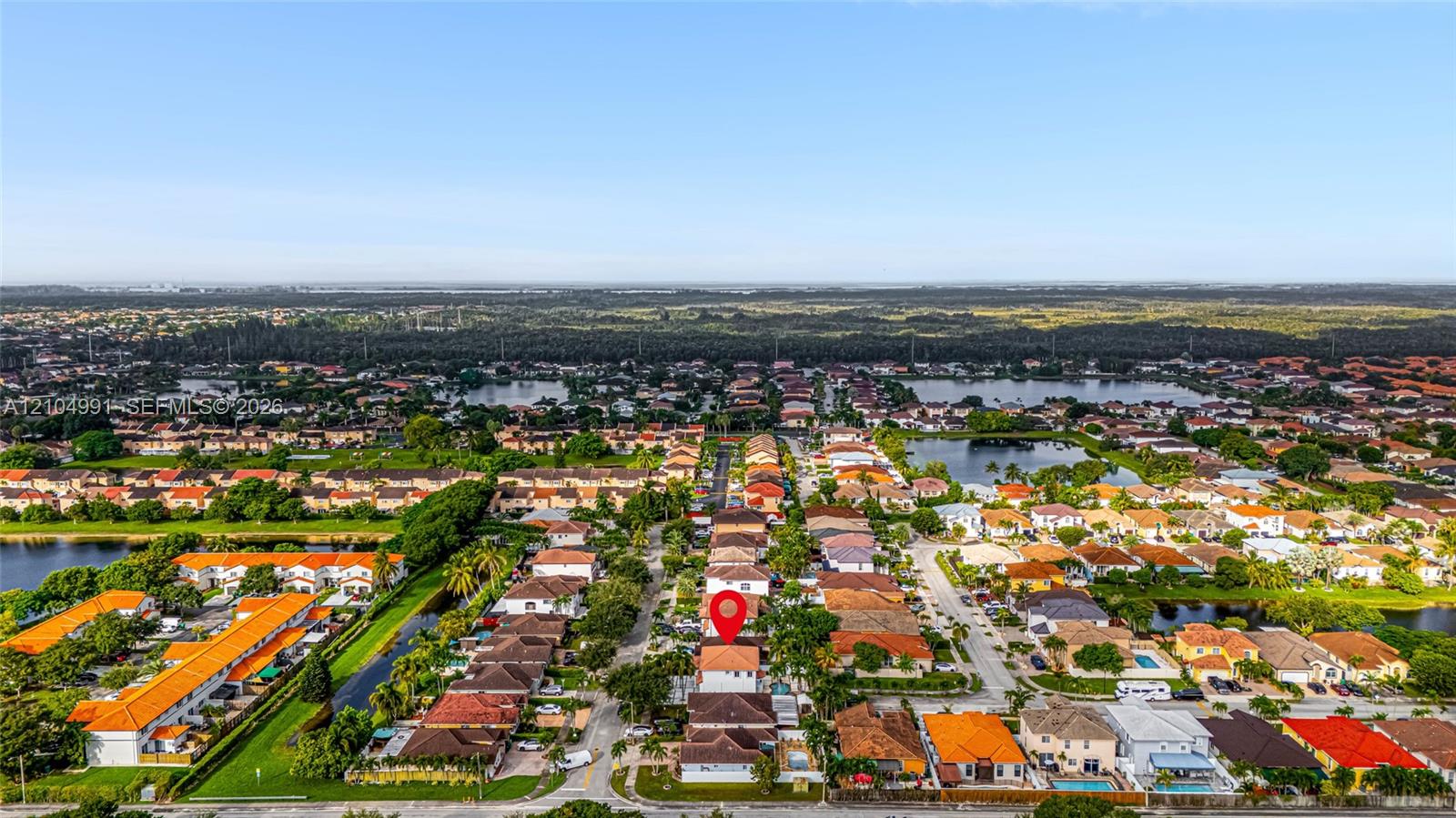 Aerial perspective of a multi-story residence featuring a tile roof, paved driveway, and perimeter fencing within a suburban development