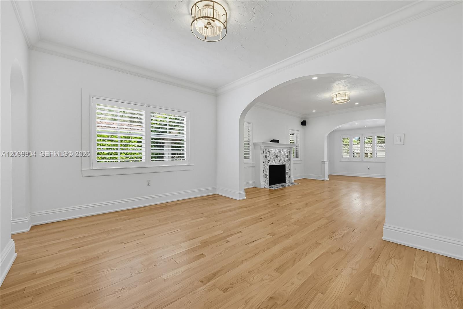 Interior featuring wood-finish flooring, decorative arched entryways, a fireplace with patterned tile surround, plantation shutters, and recessed ligh