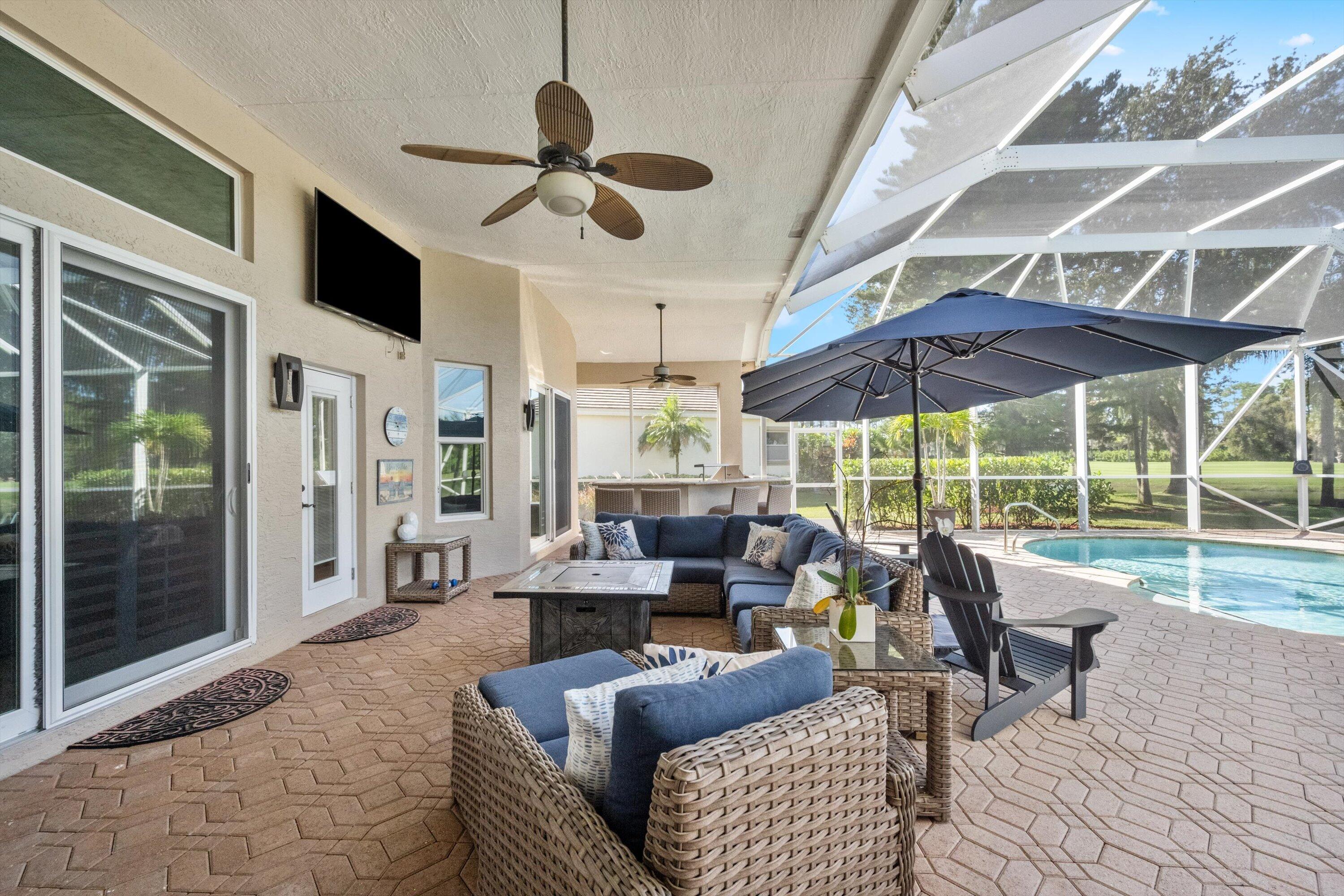 Covered lanai featuring paver flooring, ceiling fans, built-in outdoor kitchen, and a screened-in pool enclosure