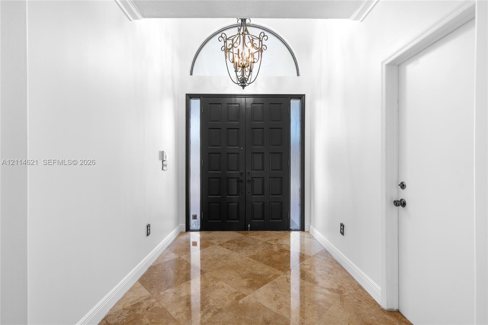 Foyer featuring double entry doors with vertical glass sidelights, an arched transom window, a multi-tiered metal chandelier, and diagonal-set stone-f