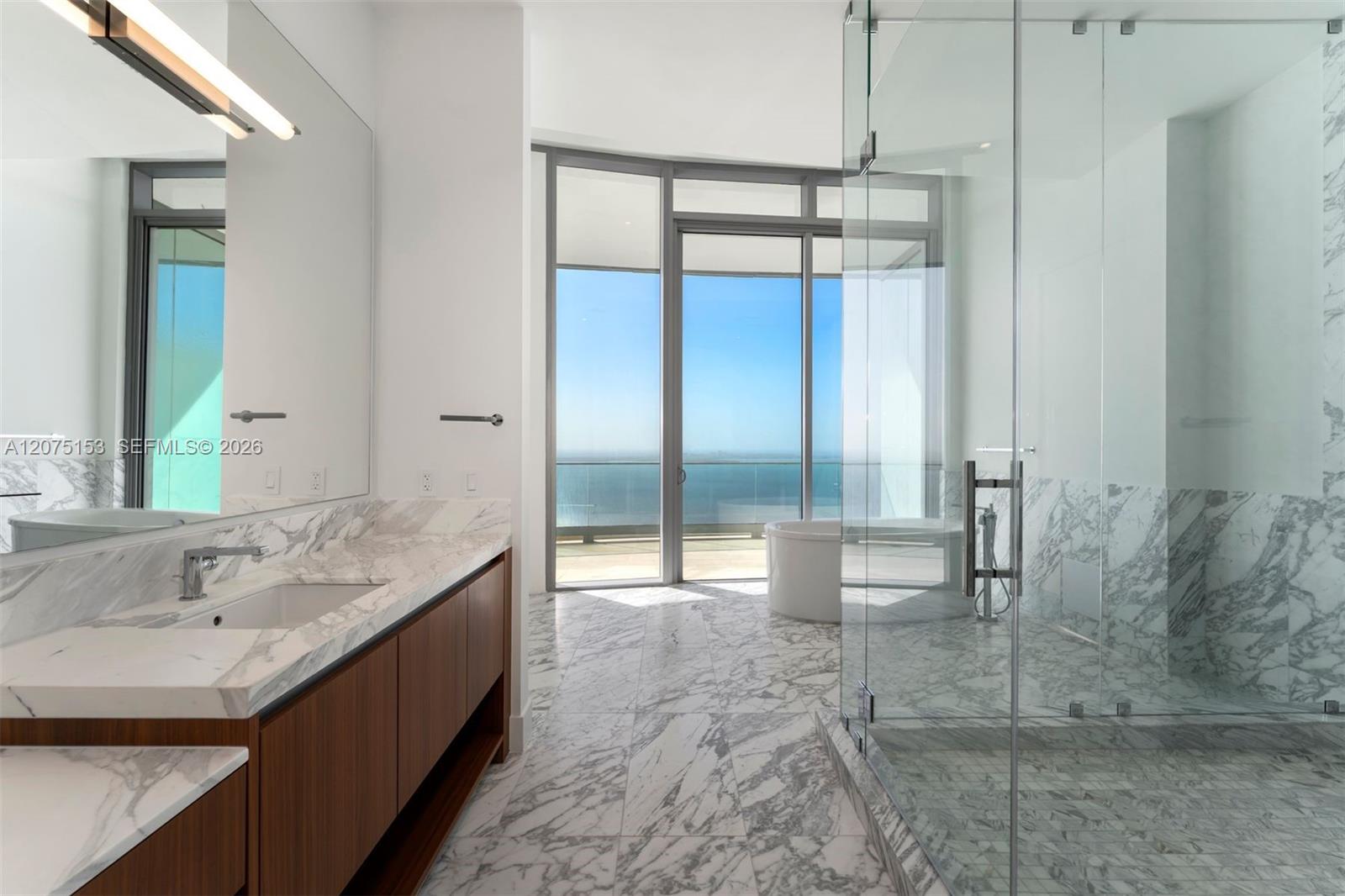 Bathroom featuring stone flooring, a wood-finish vanity with a stone countertop, a glass-enclosed walk-in shower, a freestanding soaking tub, and floo